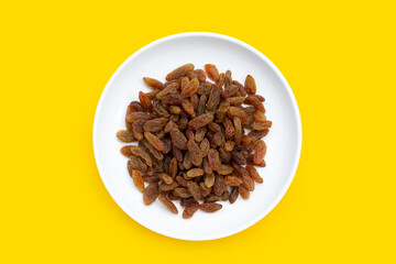 Dried grape raisins in white plate on yellow background