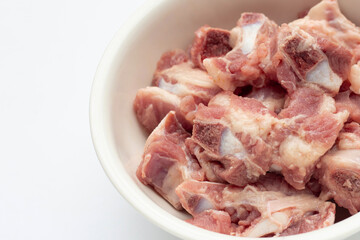 Raw pork ribs in white bowl on white background.