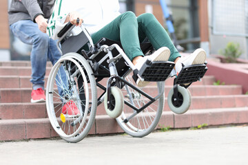 Man lifts wheelchair up steps with woman closeup