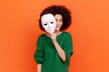 Woman with Afro hairstyle in green sweater removing white mask from face showing his smiling...