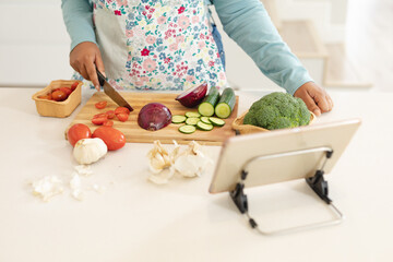 Midsection of african american plus size woman cutting vegetables, using tablet in kitchen