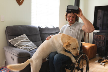Caucasian disabled man wearing vr headset sitting on wheelchair touching his dog at home