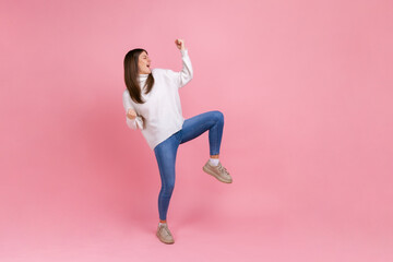Full length portrait of extremely happy female celebrating her success, standing with clenched...