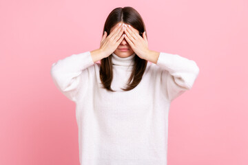 Brunette young adult female standing, covering eyes with both hand, refusing to watch, shame...