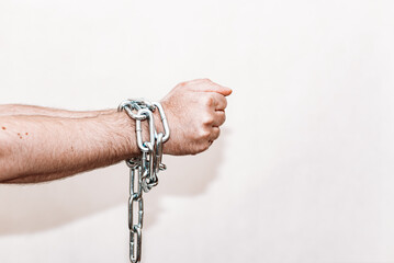 Men's hand in a steel chain.Steel chains in the hands of man on a gray wall background.Toned.Closeup,selective focus.Copy space.