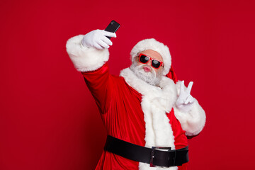 Photo of funky handsome santa claus wear red costume hat eyewear showing v-sign tacking selfie lips pouted isolated red color background