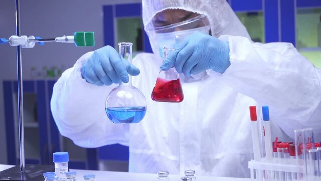 Indian scientist shaking samples in flasks and taking clipboard in lab