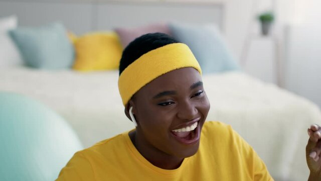 Cheerful overweight black woman dancing while listening music in airpods at home