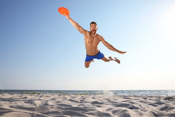 Sportive man jumping and catching flying disk at beach