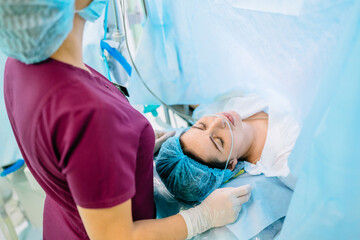 Female octors anesthetist are using tools to anesthesiologist procedures on female patient in the anesthetic machine inside operating room. Cesarean with epidural anesthesia. - obrazy, fototapety, plakaty