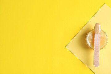 Spatula with wax on yellow background, top view. Space for text