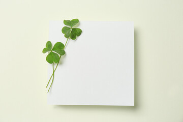 Green clover leaves and blank card on light background, top view. Space for text