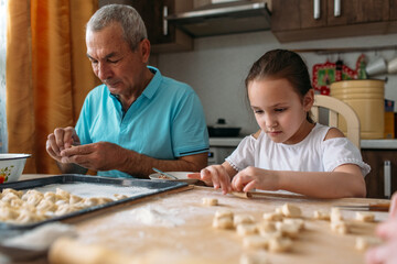 family traditions, grandfather and granddaughter make dumplings together at the table, grandfather helps granddaughter