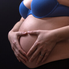 Young pregnant woman making heart with her hands, closeup
