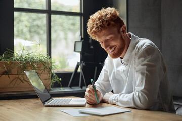 Young red head man using notebook at wooden desk