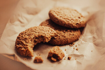 Three oatmeal round delicious cookies lie on beige wrapping paper. One of the cookies is bitten. Homemade cakes. Healthy sweets.