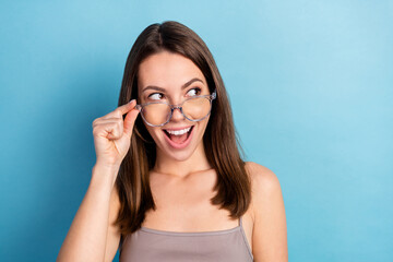 Fototapeta premium Photo of cute impressed young lady wear grey top arm glasses looking empty space smiling isolated blue color background