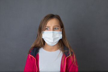 Portrait of a young angry girl with read sweater in a medical mask on grey background.