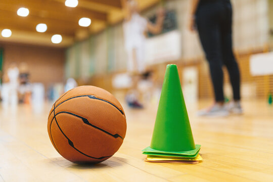 Basketball Training Equipment on Sports Court Wooden Parquet - Basketball Floor. Basketball Training Game.  Close Up on Cones and Ball with Blurred Players and Coach Playing Basketball Practice Game