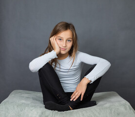Portrait of a young girl sitting on pillow with hand on her face on grey background with space for text - 463814627