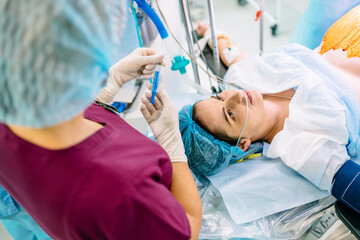 Anesthesia is administered through a syringe. Medical background. Medical doctor giving patient anesthesia before surgical operation inside modern hospital. Focus on doctor hand holding syringe - obrazy, fototapety, plakaty
