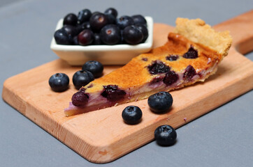 Slice of Blueberry tart on wooden cutting board. Sweet blueberry cake on a table. Homemade dessert close up photo. Healthy eating concept. Grey background with copy space. 
