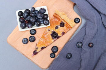 Slice of Blueberry tart on wooden cutting board. Sweet blueberry cake on a table. Homemade dessert close up photo. Healthy eating concept. Grey background with copy space. 