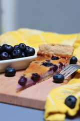 Slice of Blueberry tart on wooden cutting board. Sweet blueberry cake on a table. Homemade dessert close up photo. Healthy eating concept. Grey background with copy space. 