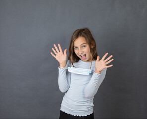 Portrait of young smiling girl giving up with medical mask on her hands on grey background. - 463816037