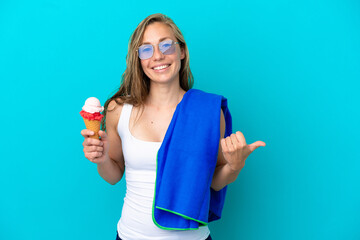 Young caucasian woman holding ice cream and wearing a beach towel isolated on blue background pointing to the side to present a product