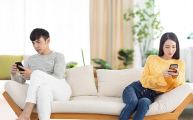 Young couple sitting on sofa using smartphone and ignoring each other.