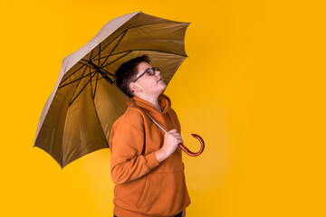 handsome boy with glasses in a brown sweatshirt under the umbrella on a yellow background