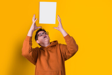 handsome boy with glasses in a brown sweatshirt holding a box in an air on a yellow background
