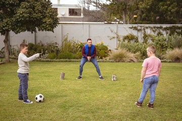 Caucasian father and two sons playing football together in the garden