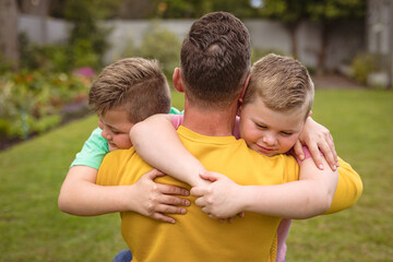 Fototapeta na wymiar Close up view of caucasian father hugging his two sons in the garden