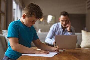 Caucasian father using laptop while son doing his homework at home