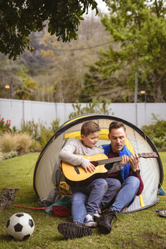 Caucasian father and son playing guitar together while sitting in a tent in the garden
