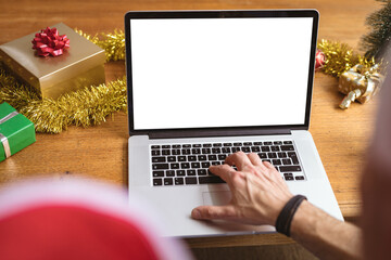 Mid section of man wearing a santa hat using laptop with copy space at home during christmas