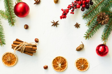 top view of the white Christmas background with spruce branch, jagdas, red balls, orange slimes, cinnamon and anise stars. flat layout.