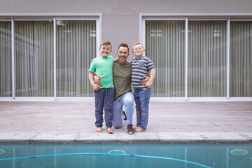 Portrait of caucasian father and two sons holding hands smiling while standing near the pool