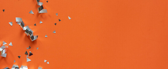 close up on group of silver color of rolling ribbon and confetti on panoramic orange background with copy space for merry christmas ,happy new year ,festival ,birthday and anniversary, concept design	