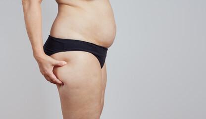 Side view of plump faceless woman in underwear touching fat on her thigh