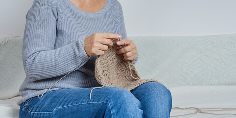 Fototapeta premium faceless woman in a gray sweater knits, sitting on a sofa, close-up with a copy space