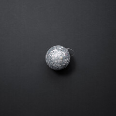 A shiny silver Christmas tree ball covered with sequins lies on a black background. Christmas decor
