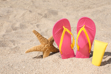 Stylish flip flops, sun protection cream and starfish on sand, space for text