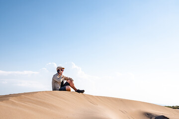 Man calling with a smart phone sitting in the desert dunes alone. Copy space