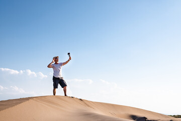 Fototapeta na wymiar Man filming himself with his cell phone in the desert dunes. Traveling male content creator