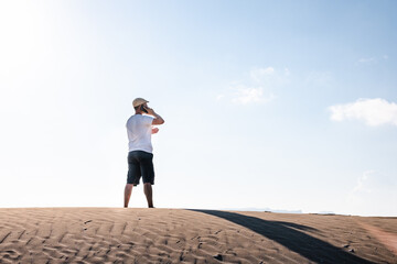 Man calling with a smart phone stand in the desert dunes alone. Copy space