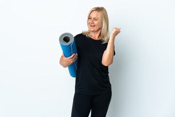 Middle age woman going to yoga classes while holding a mat isolated on white background celebrating a victory