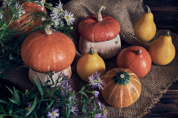 Pumpkins and a bouquet of wildflowers lie on rough burlap on a wooden background.